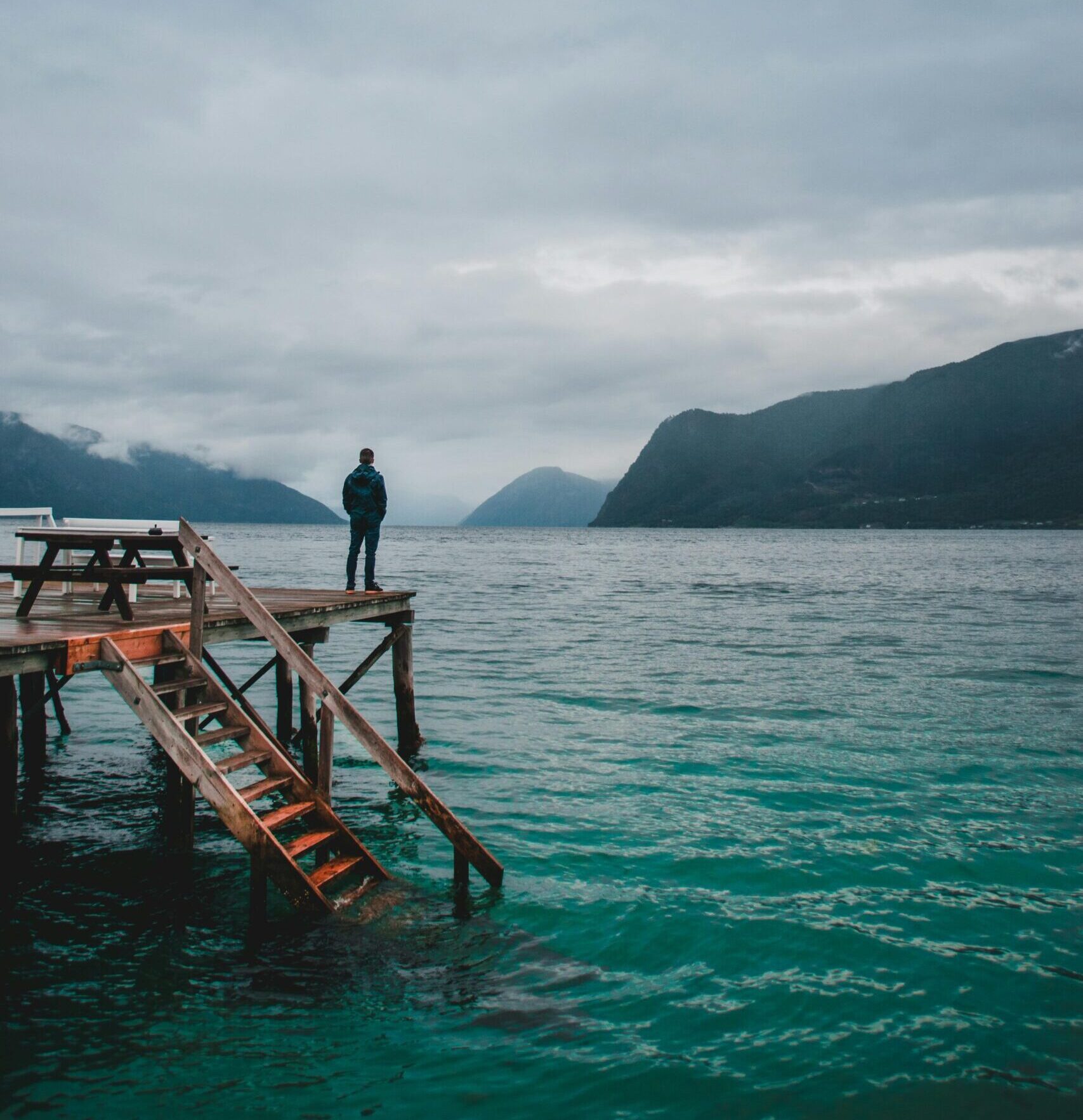 Back view of unrecognizable male tourist standing on wooden pier with stair near sea with turquoise rippling water and admiring picturesque view